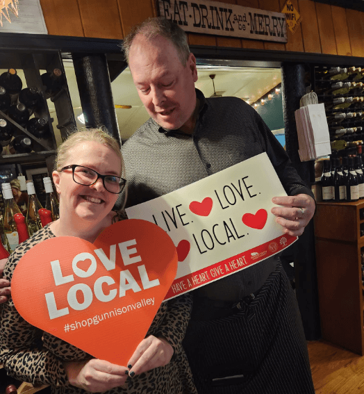 Erika, general manager at Garlic Mike's, holds a die-cut heart that says "Love Local #shopgunnisonvalley"